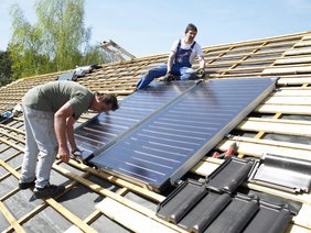 Arbeiter bei der Montage eines Solarkollektors auf dem Dach